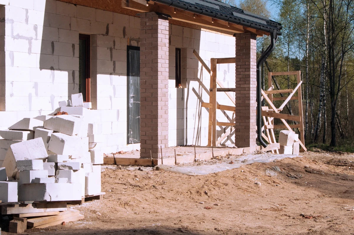 Stan surowy zamknięty: elewacja domu w budowie z murowanymi filarami, ścianami z bloczków i rusztowaniem