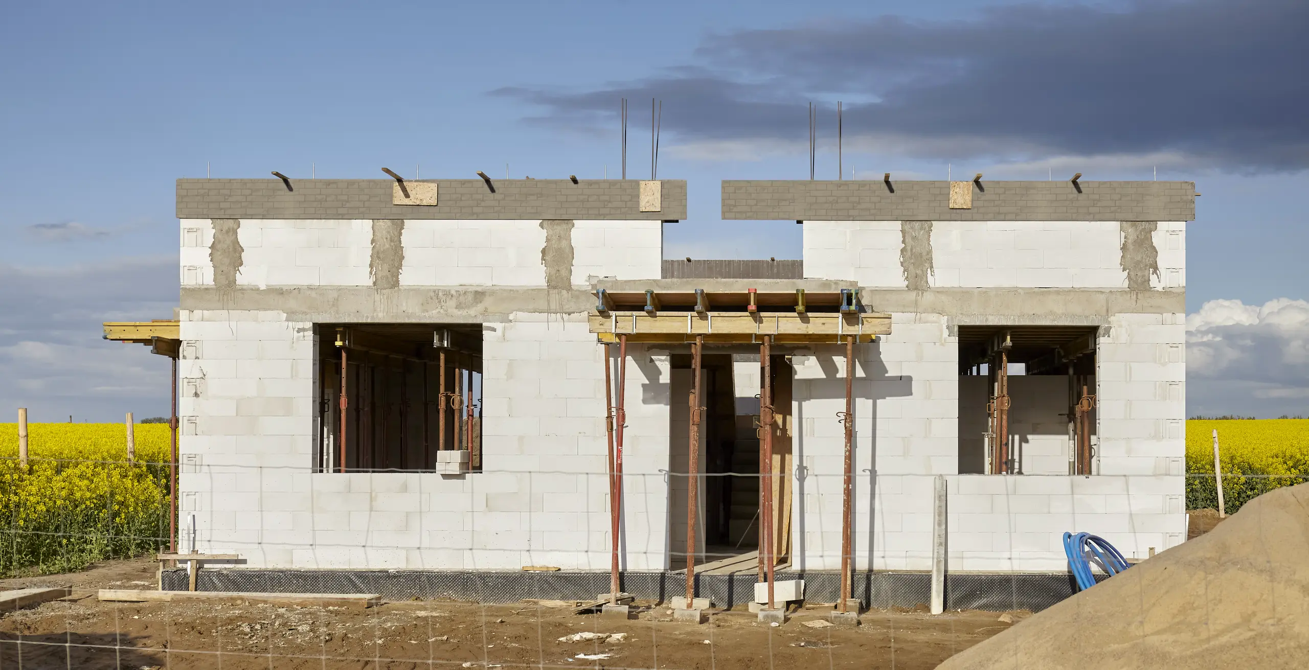 Biały dom w stanie surowym otwartym z widocznymi ścianami nośnymi, belkami żelbetowymi i podporami stropowymi