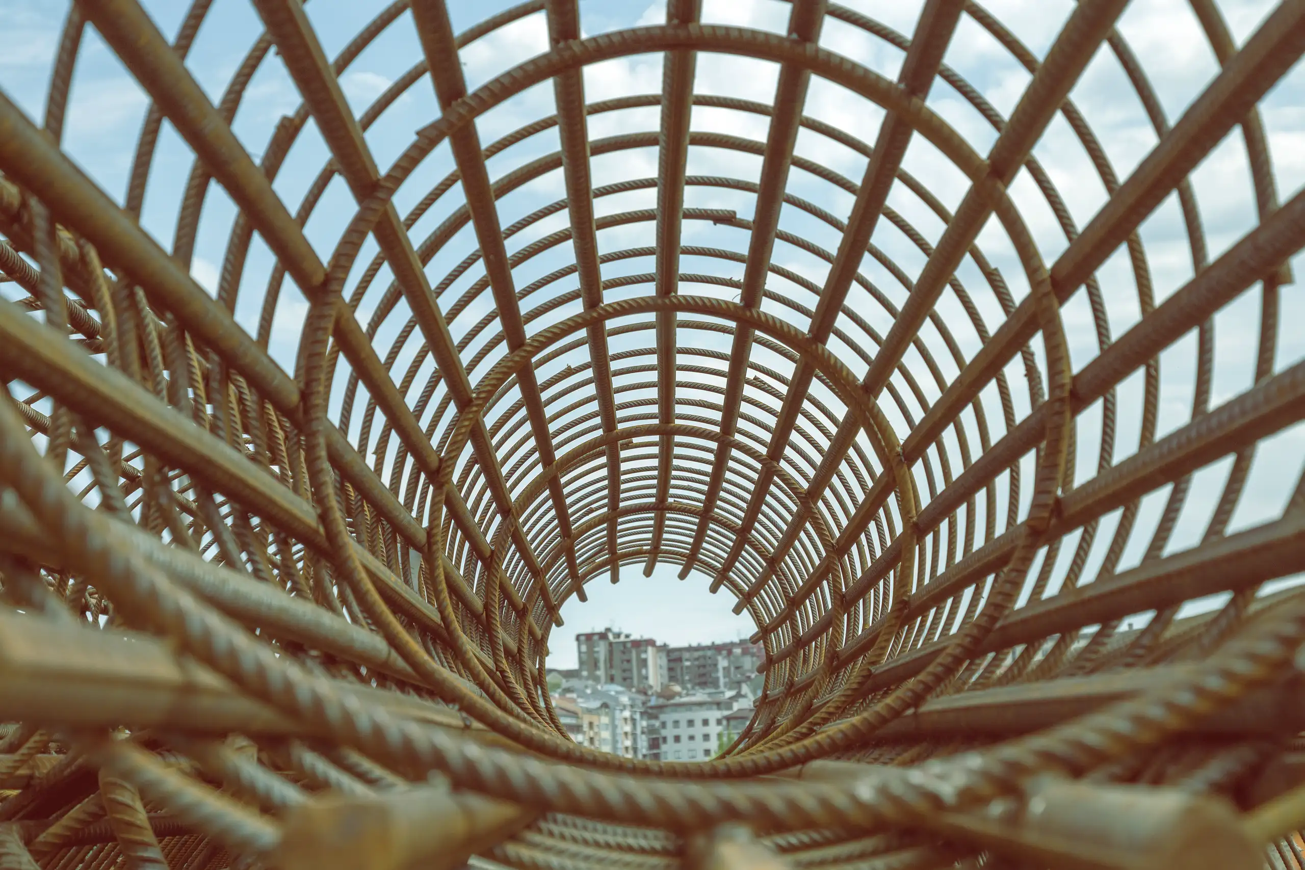 Zbrojenie fundamentów: stalowa klatka z prętów zbrojeniowych w kształcie cylindra na tle zabudowy miejskiej